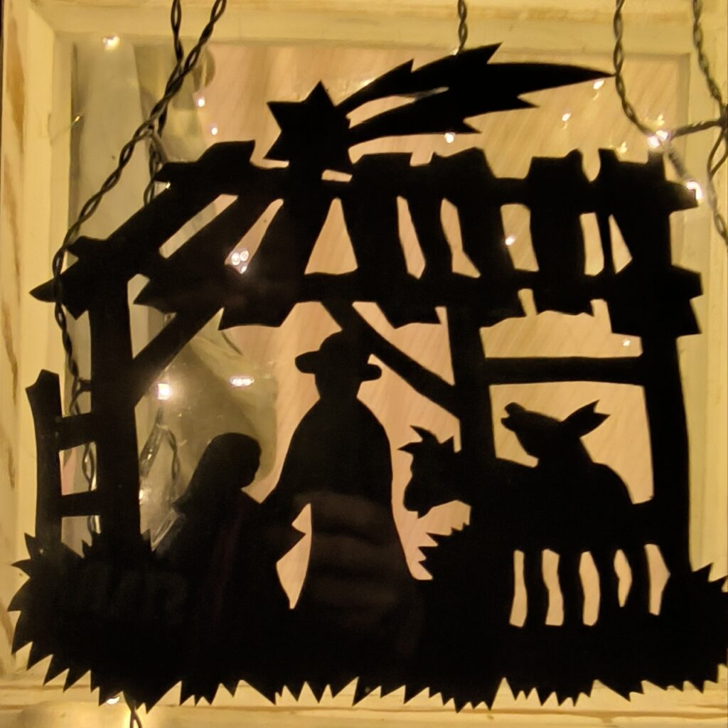 Scherenschnitt einer Krippe mit Maria, Josef, Ochse, Esel, Stall und Stern beleuchtet mit elektrischen Kerzen